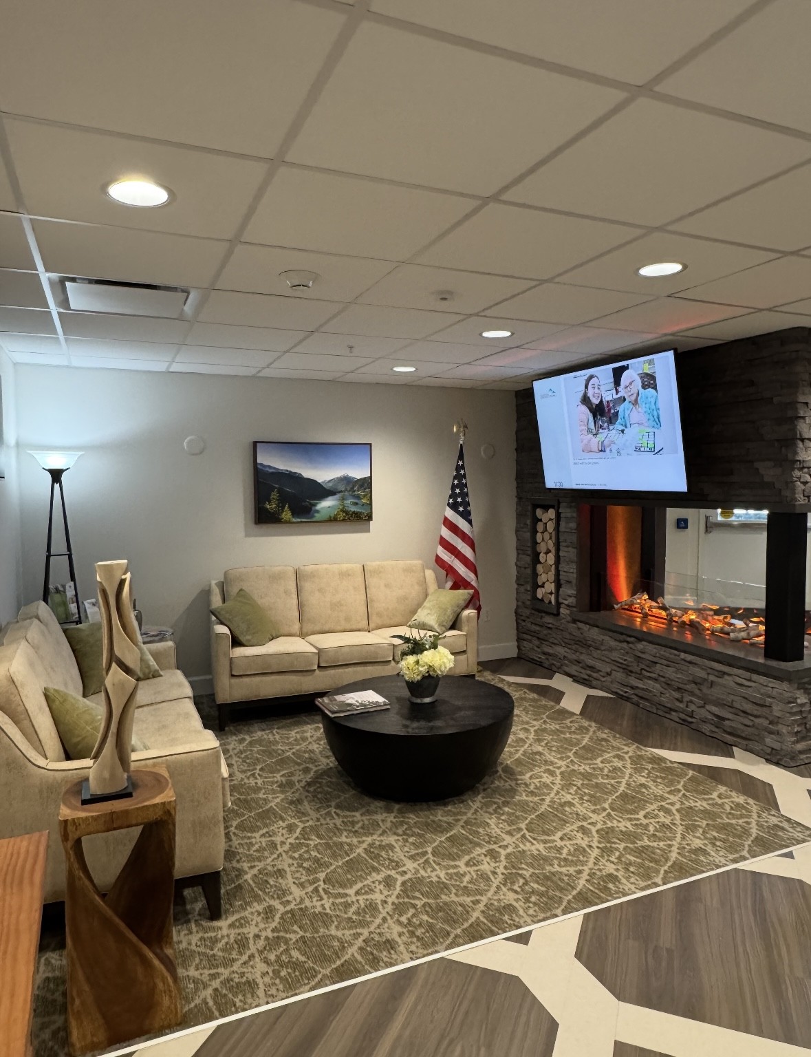 Lounge at Cascade Valley Senior Living with cream sofas around a round coffee table, an American flag and a stacked stone fireplace